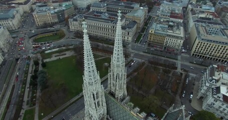 High-angle aerial view of a grand European city  Vienna featuring the prominent twin Gothic spires of a historic church Votivkirche towering over dense surrounding classical architecture and city stre