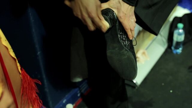 Detailed close-up shot of a professional male ballet dancer using a tool (or chalk) to scuff or prepare the sole of his ballet shoe or pointe shoe just before going on stage