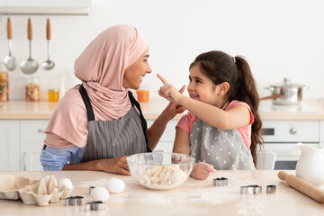 A mother and her daughter share a joyful moment while baking cookies. They are smiling and engaged, surrounded by baking ingredients in a bright kitchen.