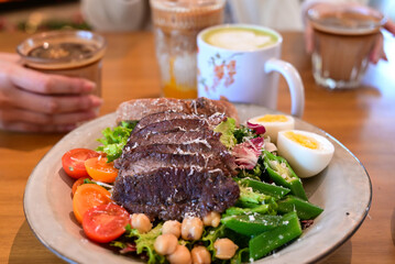 Healthy steak salad brunch with coffee drinks - Colorful plate of steak salad with eggs, chickpeas, and vegetables served with coffee and matcha latte in a cozy café