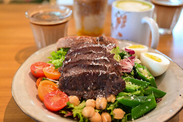 Healthy steak salad brunch with coffee drinks - Colorful plate of steak salad with eggs, chickpeas, and vegetables served with coffee and matcha latte in a cozy café