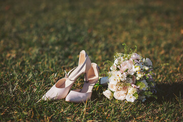 Pink shoes and a bridal bouquet on green grass during a wedding ceremony in a park setting at...