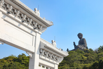 Entrance gate to Tian Tin monastery and the Big Buddha on the mountain behind at Ngong Ping village on Lantau Island, Hong Kong, China.