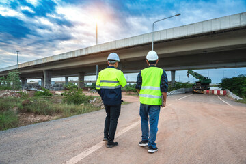 Workers in Safety Gear Assess Large Construction Project Under Elevated Highway at Dusk