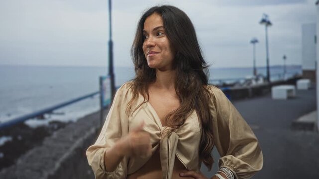 Woman showing cleavage and pointing thumb to the side on street promenade by the sea; joy holiday confidence.