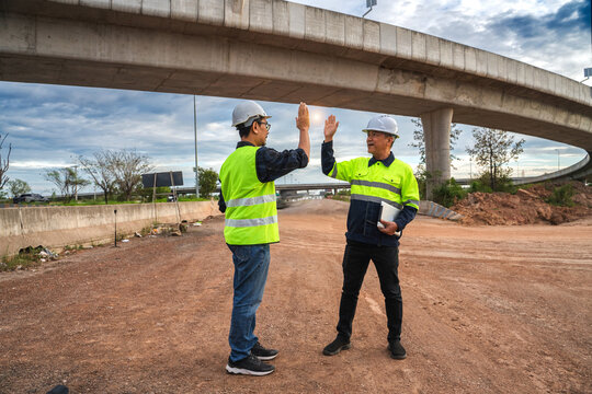 Two Construction Workers High-Fiving Under a Bridge on a Construction Site During Sunset