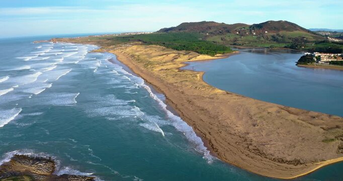 Dynamic aerial footage showcasing the long sandspit of Liencres beach (Valdearenas), ocean swells crash along the coast in the River Pas in Mogro (Cantabria)