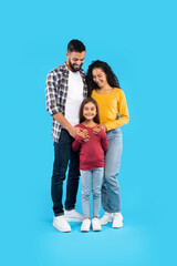 A father and mother stand close together, embracing their young daughter who smiles widely. The bright blue background emphasizes their unity and happiness.