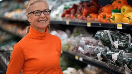 A mature woman smiles as she checks prices in the produce section while grocery shopping during the day.