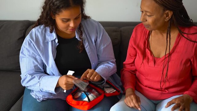 African daughter using first aid kit to help her mother at home - Family, lifestyle and healthcare concept