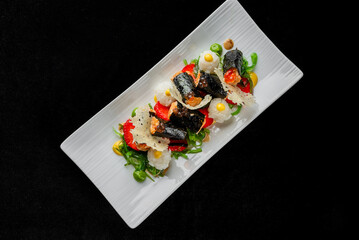 A gourmet dish featuring modern maki rolls and rice balls with fish and vegetables, plated artistically on a white rectangular dish.