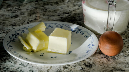 Blocks of butter and a brown egg on a plate with a cup of milk nearby