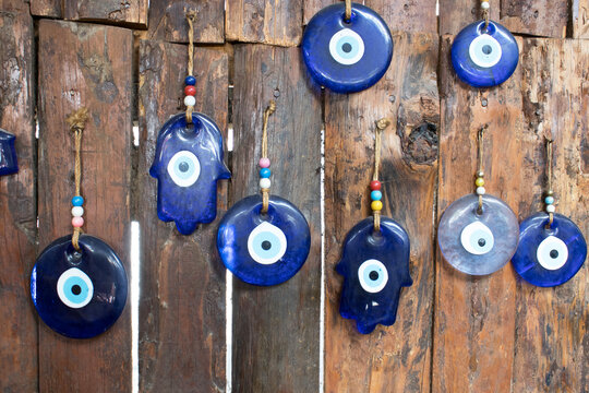 Blue glass evil-eye and hamsa charms hanging on a rustic wooden fence. Traditional Turkish protection symbols; artisan craft and travel decor concept.
