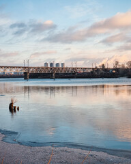 Old railway bridge over the river at sunrise. Truss bridge over the river in rays of rising sun, silhouettes of skyscrapers in the background. 
