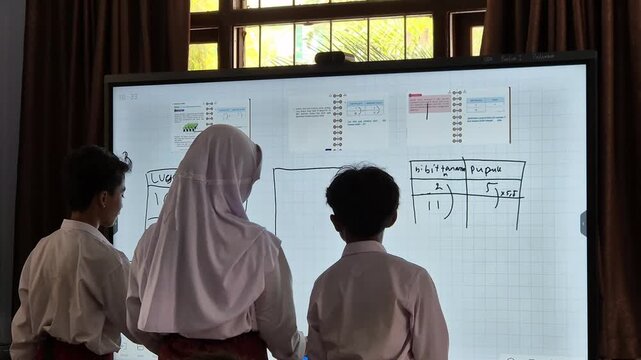 Three elementary school students working on math problems on a digital screen board in the classroom. Pamekasan, Indonesia - Dec 09, 2025.