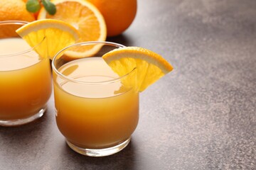 Fresh orange juice in glasses and fruits on grey table, closeup. Space for text