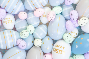 Mix of colorful Easter eggs and colorful quail eggs on pastel coloured wood as a background. On some eggs are texts "Happy Easter". 