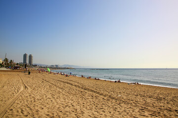 Beautiful golden sand,  clear blue sky and buildings of the city in the background on Barceloneta Beach, on a lovely summer day, Barcelona, Catalonia, Spain.