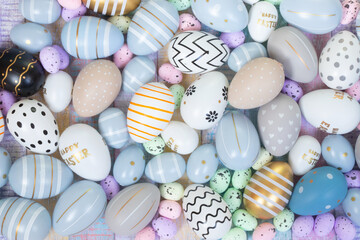 Mix of colorful Easter eggs and colorful quail eggs on pastel coloured wood as a background. On some eggs are texts "Happy Easter". 