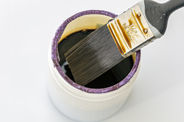A close-up photograph shows a paint brush with a black handle and metal ferrule immersed in an open can of lacquer.