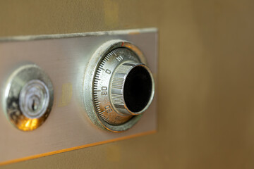 Close-up image of an old metal safe combination dial and key lock on a vintage beige safe door with visible rust and wear.