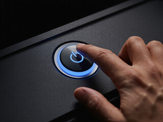 Close-up of a human finger pressing a glowing blue power button on a dark electronic device.