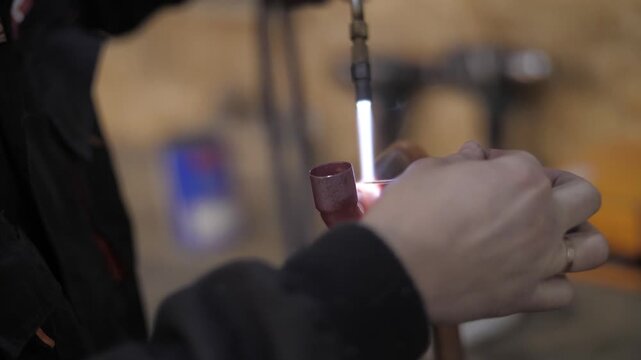 Plumber soldering copper pipe with blowtorch in workshop.
