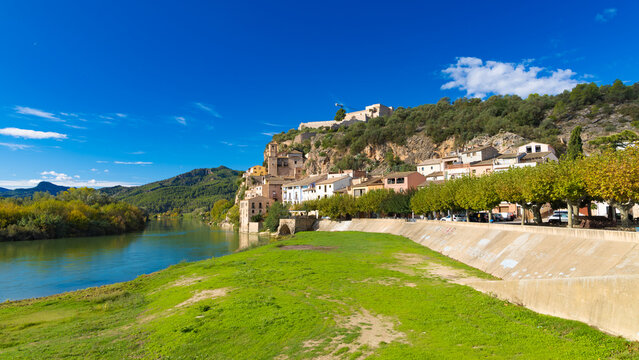 Scenic view of Miravet village and castle by the Ebro river in Catalonia, Spain, with green grass and blue sky.