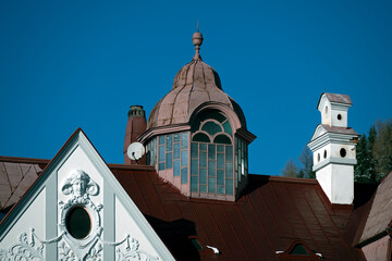 House roof with brick chimney stack and attached historic gable turret against a blue sky in Mariazell, Austria;