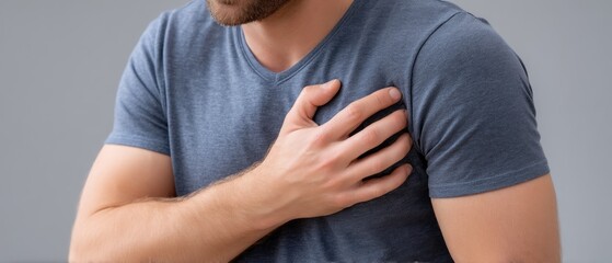 Man holds chest in pain, showing signs of possible heart attack or angina pectoris against a plain background, highlighting issues in healthcare and human emotion