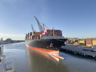 Massive gantry cranes lift and move containers for loading and unloading. Photo of a large container ship moored at a port berth during active cargo operations. container terminal. ship's bulb forward