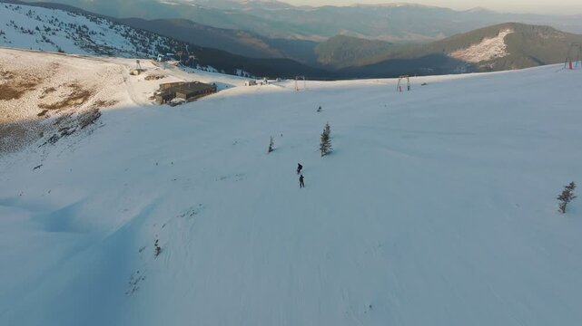Gentle slopes and bright winter sunshine illuminate skiers, Elevated view depicts carefree skiers amid snowy terrain with peaceful sunlight and distant valley in sight