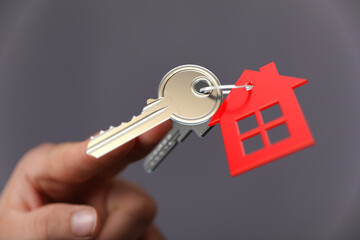 A close-up shot features a hand holding house keys with a red house-shaped tag. This image represents homeownership, real estate, and the concep