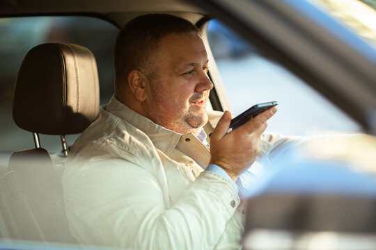 Adult man using voice assistant on phone in car, focused