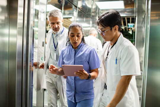 Adult and mature medical team reviewing tablet in hospital elevator, focused