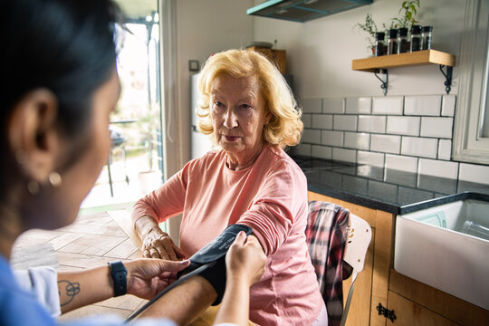 Senior woman serious as adult caregiver checks blood pressure at home