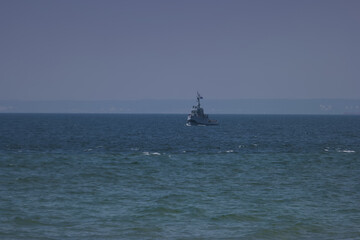Navy vessel patrols calm waters near coastal horizon during bright sunny day