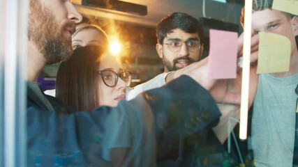 Coworkers adjusting sticky notes on glass board. Woman studying layout while men arranging details. Team shaping project workflow during collaborative planning inside stylish office room.