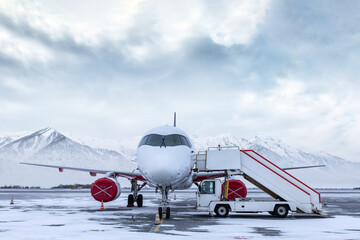 White passenger plane with boarding stairs on the winter airport on the background of high snow capped mountains