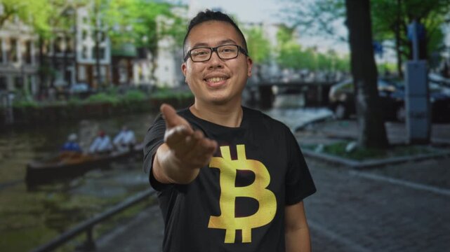 Man in bitcoin t shirt with hand extended for handshake on street in amsterdam; crypto trust friendly.