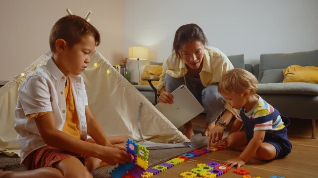 Young smiling mother and her two sons playing with a colorful constructor puzzle on the floor in the living room, enjoying a creative and educational activity together on a family weekend