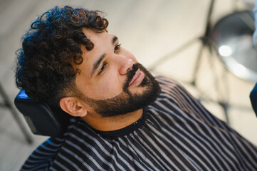 Man with curly hair getting beard trim in barbershop