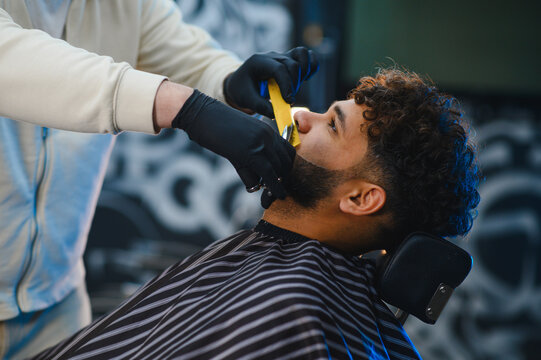 Barber shaving man's beard in professional barbershop - Powered by Adobe