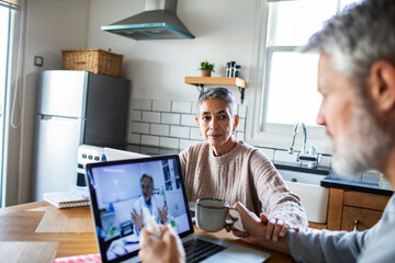 Senior couple on telehealth video call in home kitchen, concerned