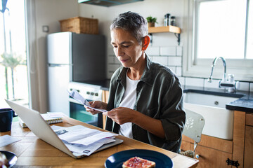 Mature woman reviewing bills in home kitchen, focused and concerned