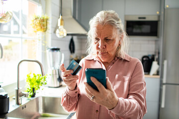 Senior woman concerned with credit card payment on smartphone at home kitchen