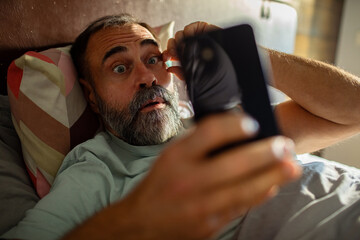Mature man shocked by smartphone in bed at home
