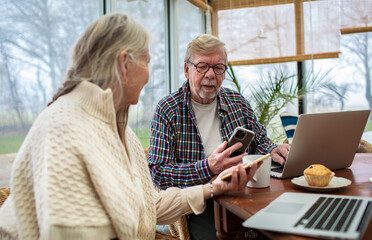 Senior couple focused on smartphones and laptops in home sunroom