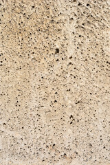 A close-up, vertical full-frame background of a light beige, rough porous stone surface characterized by numerous small, dark holes