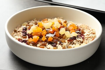 Making granola. Bowl with oat flakes, honey and dried fruits on grey table, closeup